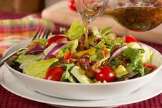 a person pouring dressing on a salad in a bowl with tomatoes and lettuce