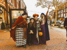 three women dressed up as witches pose for a photo on the sidewalk in front of a store