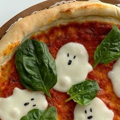 a pizza topped with cheese and spinach on top of a wooden cutting board covered in fake ghost faces