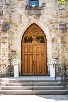 the entrance to an old stone church with two wooden doors and flowers in front of it