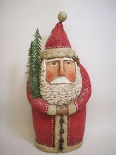 a santa clause figurine with a tree in his lap and wearing a red hat