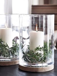 two clear vases with candles and greenery in them on top of a table