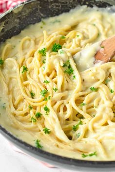 a skillet filled with pasta and sauce on top of a white tablecloth next to a wooden spoon