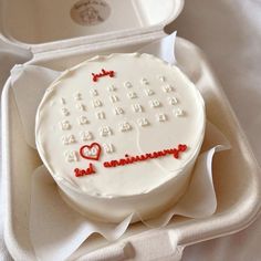 a white cake with red writing on it sitting in a box next to a container