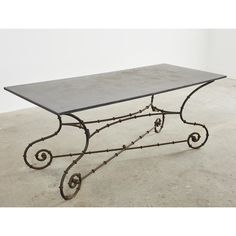 a wrought iron coffee table with grey stone top and metal base, sitting on concrete flooring