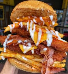 a large sandwich with meat, cheese and french fries on it is stacked high in the air