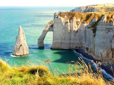 two large rocks sticking out of the ocean next to some grass and water with cliffs in the background