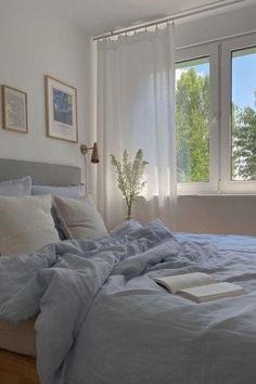 an unmade bed sitting in front of a window next to a book on top of a wooden floor