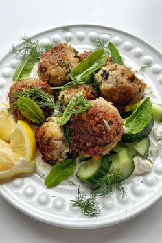 a white plate topped with meatballs and cucumbers next to lemon wedges