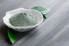 Close-up of a cosmetic dry green clay in a white bowl in the shape of a shell on a black wooden table. Decorated with green leaves. Diy Foundation, Make Your Own Clay, Mountain Rose Herbs, White Bowl, Natural Exfoliant, Homemade Face