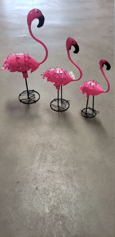 three pink flamingos sitting on top of metal stands in an empty room with concrete flooring