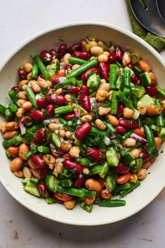 a white bowl filled with beans and veggies on top of a table next to a spoon