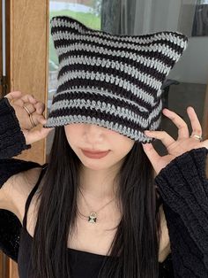 a woman wearing a black and white knitted hat holding her hands up to her face