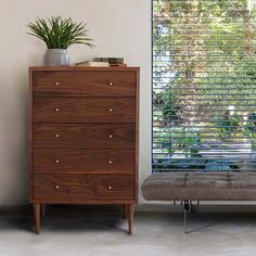 a brown chest of drawers sitting next to a window with blinds on it's side