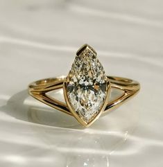 a yellow gold ring with a pear shaped diamond in the center on a white surface