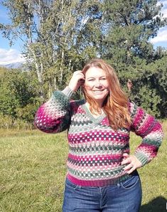 a woman standing in the grass with her hands on her head wearing a colorful sweater