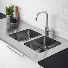 two stainless steel sinks in a kitchen with black counter tops and white tile backsplash