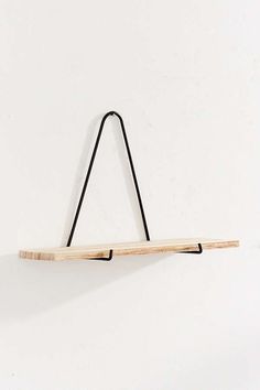 a white wall with a wooden shelf hanging from it's side and a black string attached to the top