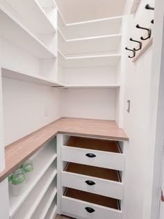 an empty walk in closet with white shelves and wooden counter tops, filled with drawers