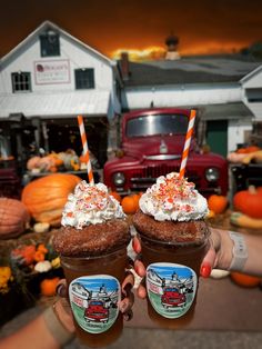 two people holding up cups with whipped cream and pumpkins in the background