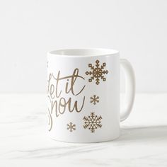 a coffee mug with the words let it snow written on it in gold and white