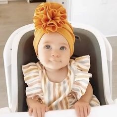 a baby sitting in a highchair wearing a yellow headband with an orange flower