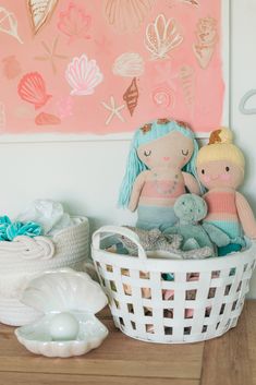 two stuffed animals sitting in a basket next to a wall with seashells on it