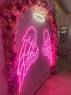 a neon sign with angel wings on it in front of pink flowers and greenery