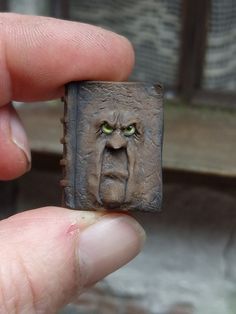 a hand is holding a small piece of metal with a face on it and green eyes