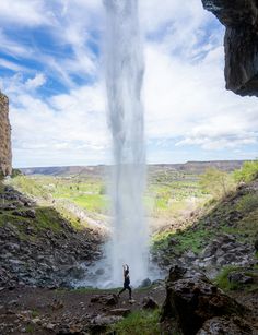 a person standing in front of a waterfall with water coming out of the ground and into the air