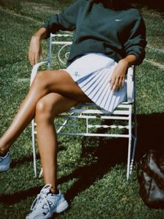 a woman is sitting on a chair in the grass with her legs spread out and wearing tennis shoes