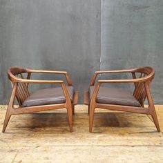 a pair of chairs sitting on top of a wooden floor next to each other in front of a gray wall