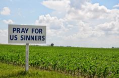 a sign that says pray for us sinners in front of a field of corn