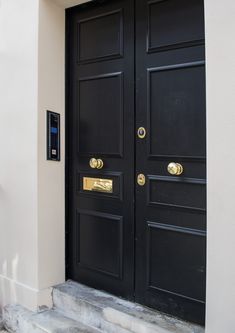 two black doors with gold handles on the side of a building and steps leading up to them