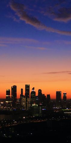 the city skyline is lit up at night with bright lights and clouds in the sky