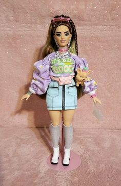 a barbie doll wearing a purple shirt and blue skirt holding a small dog in her hand