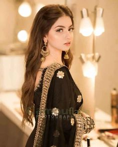 a beautiful woman in black dress standing next to a mirror and looking at the camera