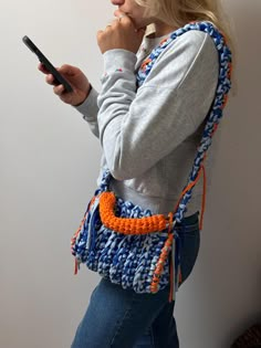 a woman holding a cell phone in her right hand and wearing a crocheted purse