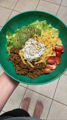 a green plate topped with lots of food on top of a tiled floor next to someone's feet