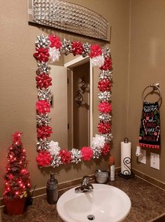 a bathroom decorated for christmas with red and silver decorations on the mirror, toilet paper roll trees
