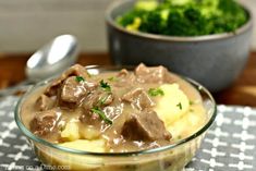 a glass bowl filled with beef and gravy on top of a checkered table cloth