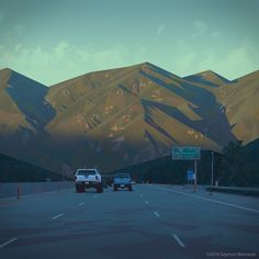 two cars are driving down the road in front of some mountain range at dusk time