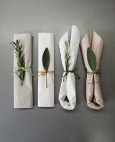 four napkins wrapped in white paper and tied with twine, each decorated with green leaves