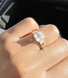 a person's hand holding an engagement ring in their left hand, while the other hand is on the steering wheel