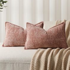 two pillows sitting on top of a white couch next to a vase with flowers in it