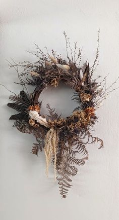 a dried wreath hanging on the wall next to a white wall with plants and leaves