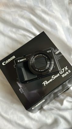 a black camera sitting on top of a white bed covered in blankets and sheets with the box open