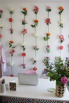 a white desk topped with a laptop computer sitting next to a flower wall covered in pink and orange flowers