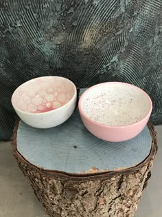 two bowls sitting on top of a piece of wood next to each other in front of a wall