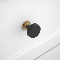 a black knob on the side of a white cabinet with brass handles and an oval handle